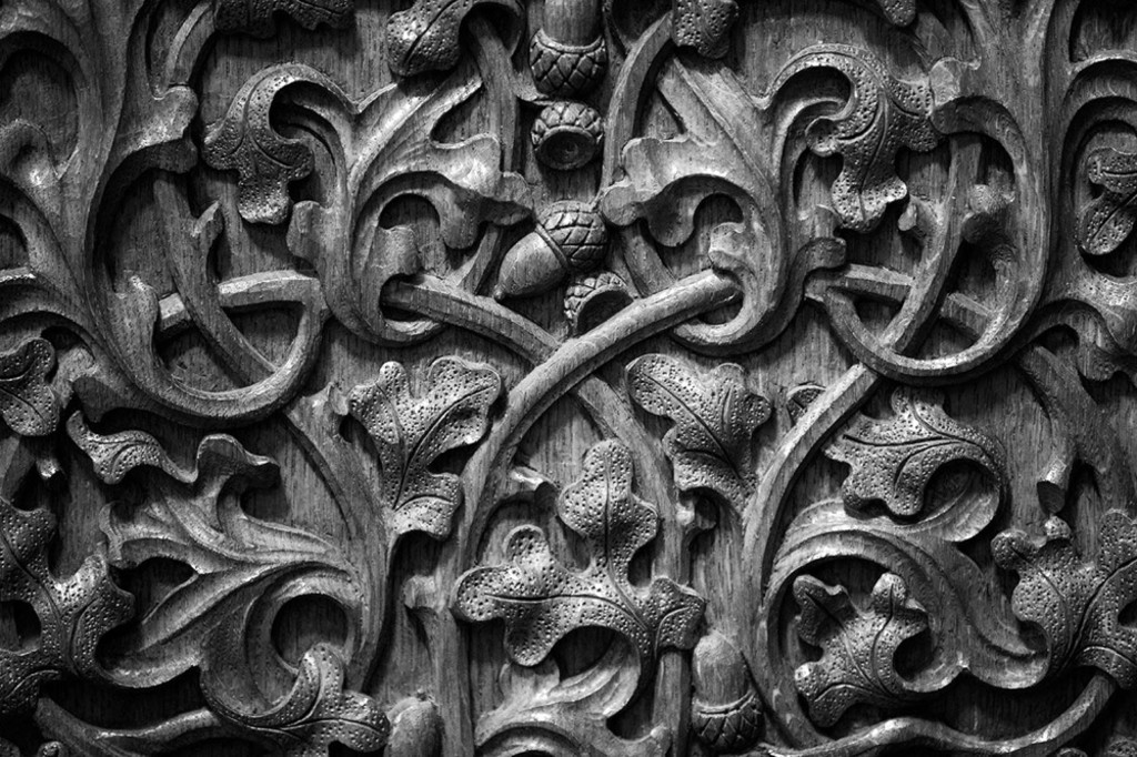 Black and white close-up photo of oak leaf and acorn shaped carvings into a wooden panel. Black and white close-up photo of oak leaf and acorn shaped carvings into a wooden panel.