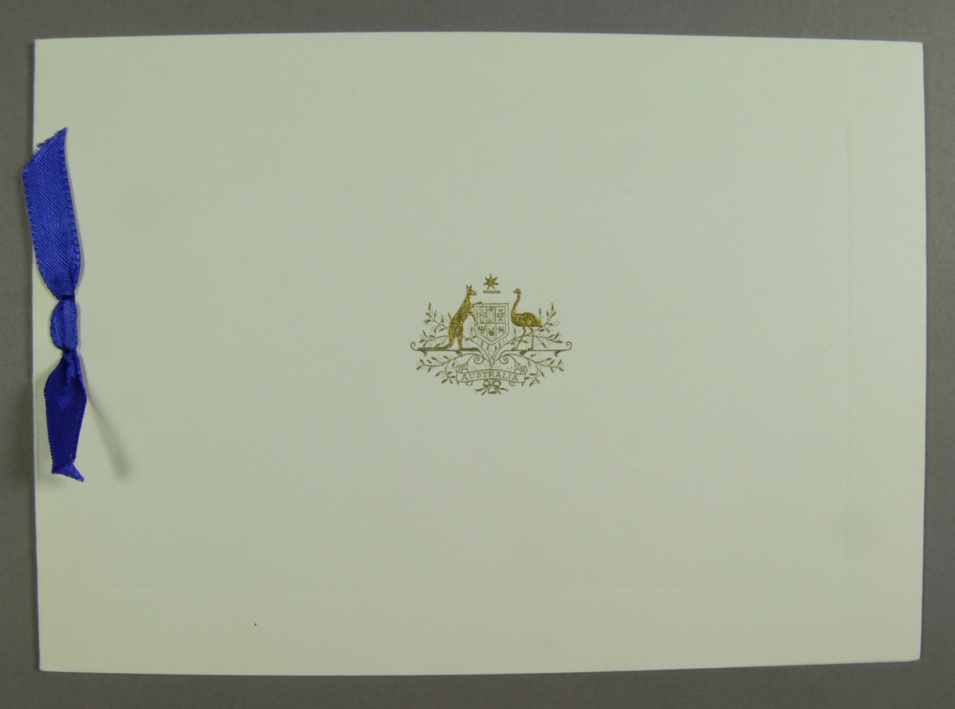 A white card cover, embossed in gold with the Australian coat of arms and bound with a blue ribbon. A white card cover, embossed in gold with the Australian coat of arms and bound with a blue ribbon.