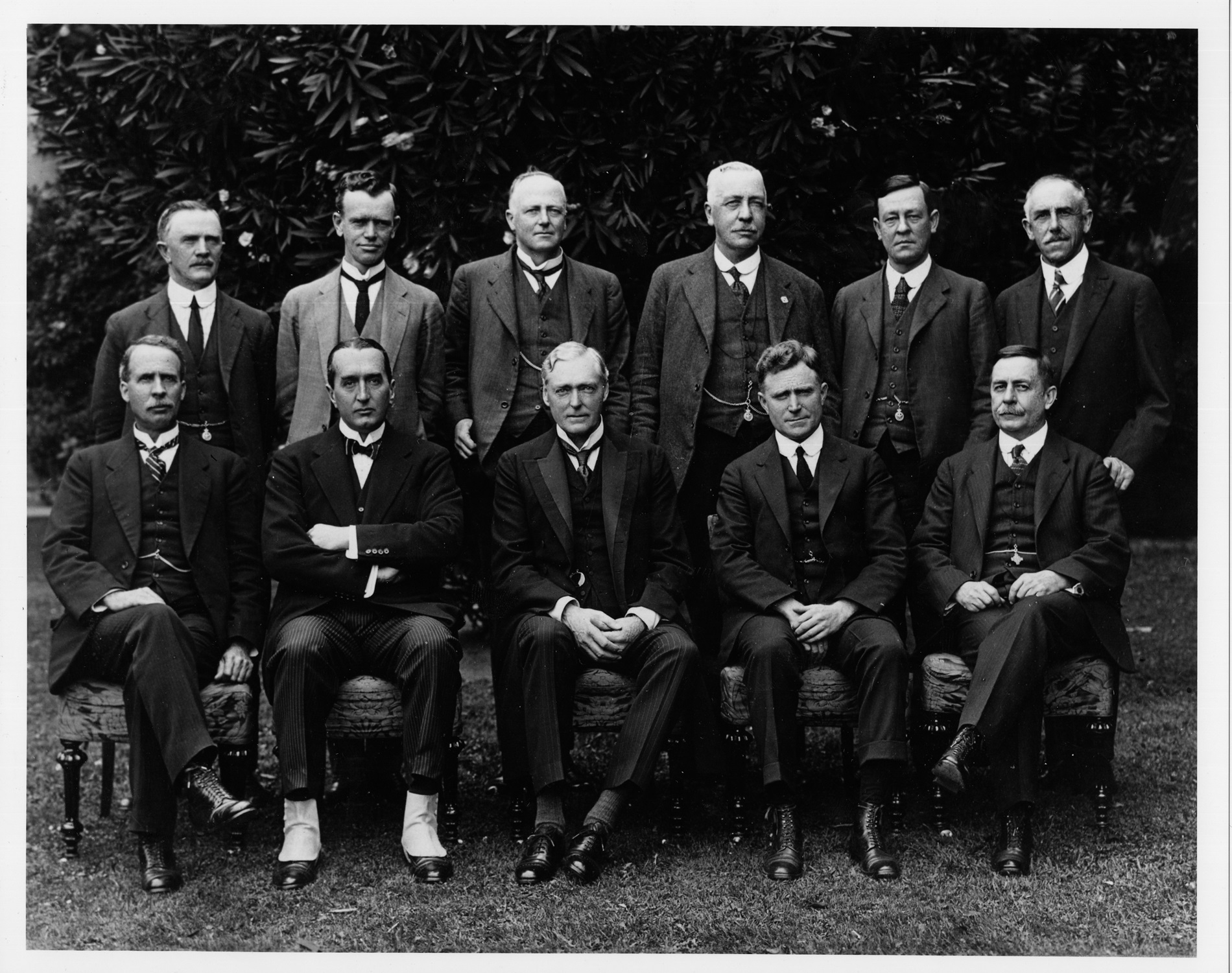Black and white photograph of eleven men, posing in two rows, all wearing three-piece suits. Black and white photograph of eleven men, posing in two rows, all wearing three-piece suits.