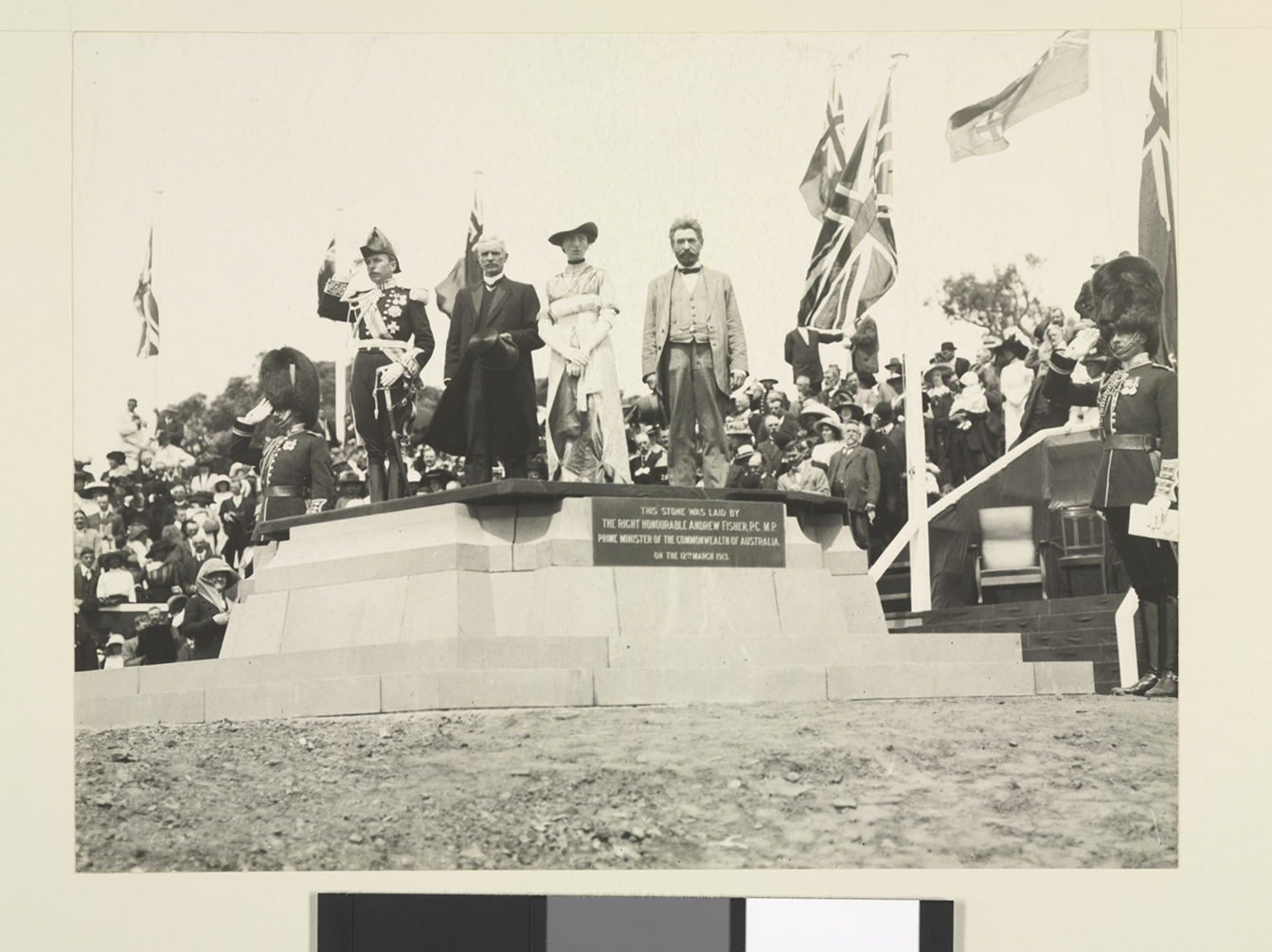 Governor-General Denman, Prime Minister Fisher, Lady Denman and King O'Malley stand on a commemorative stone. British and Australian flags are the in background, with a large crowd behind. Governor-General Denman, Prime Minister Fisher, Lady Denman and King O'Malley stand on a commemorative stone. British and Australian flags are the in background, with a large crowd behind.