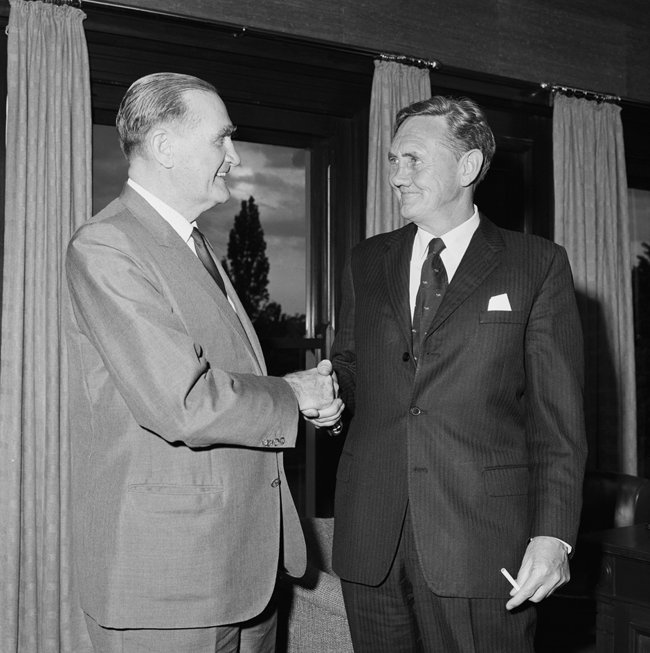 John McEwen shakes John Gorton's hand. Gorton is holding a cigarette. John McEwen shakes John Gorton's hand. Gorton is holding a cigarette.