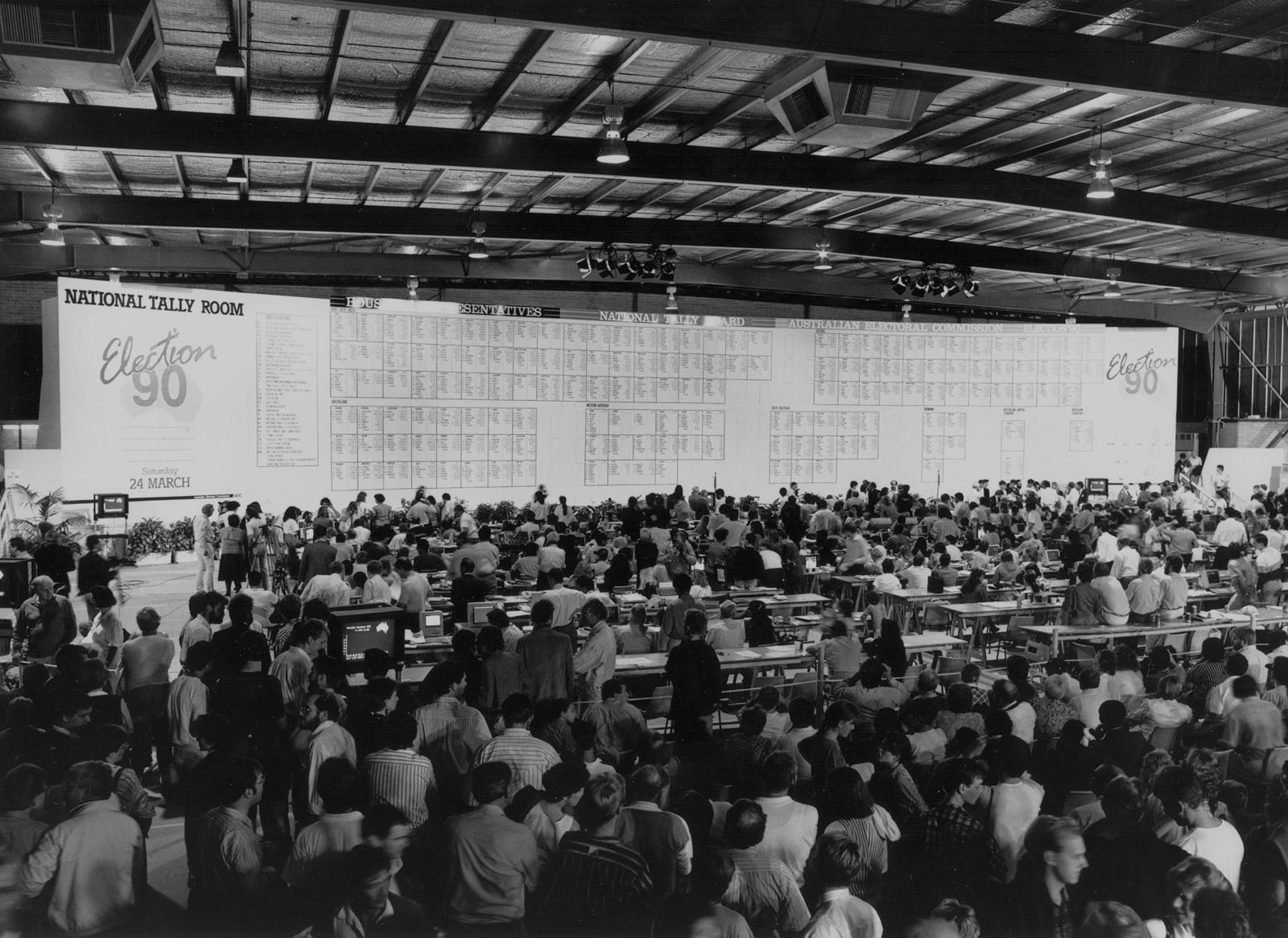A crowd of people stand in the National Tally Room in Canberra looking at the giant National Tally Room board showing the results of the 1990 election.
