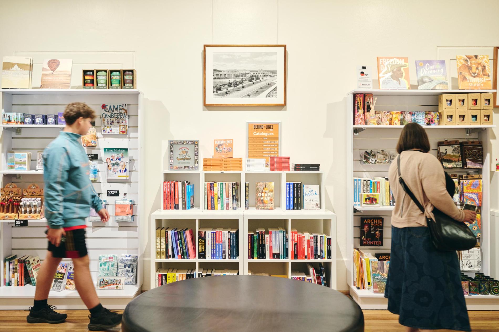 Two people browse books and other shop products on shelves.  Two people browse books and other shop products on shelves.
