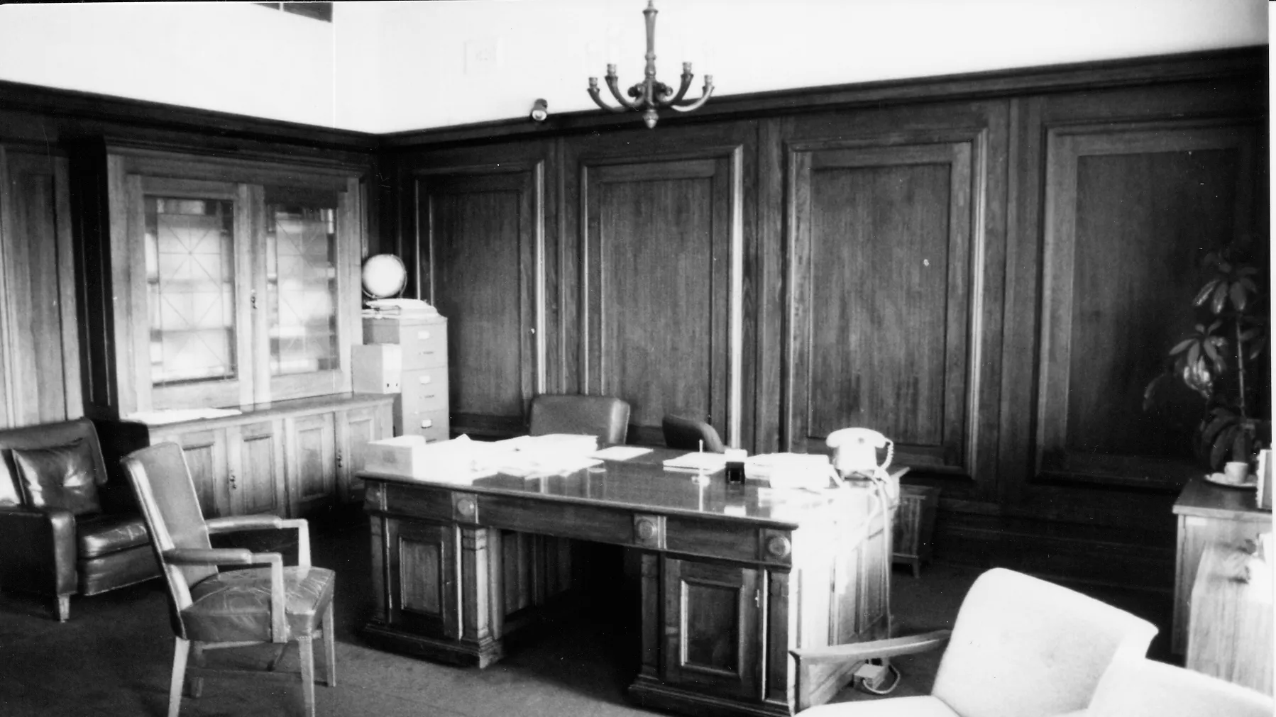 This black and white photograph shows the layout of the Clerk of the Senate’s office in 1985 when it was occupied by Alan Cumming Thom. The timber-panelled room contains a large desk (originally designed by the building’s architect, John Smith Murdoch), glass-fronted built-in bookshelves and a sideboard with an indoor plant. There are a range of visitor chairs and an easy chair in the foreground. This black and white photograph shows the layout of the Clerk of the Senate’s office in 1985 when it was occupied by Alan Cumming Thom. The timber-panelled room contains a large desk (originally designed by the building’s architect, John Smith Murdoch), glass-fronted built-in bookshelves and a sideboard with an indoor plant. There are a range of visitor chairs and an easy chair in the foreground.
