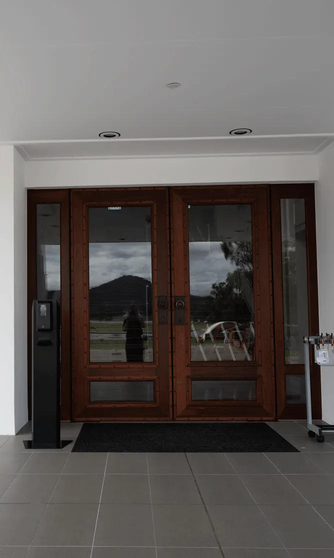 An entrance to a building with large glass double doors with wooden frames. An umbrella stand sits to the right. A black sign says 'Welcome to MoAD'. An entrance to a building with large glass double doors with wooden frames. An umbrella stand sits to the right. A black sign says 'Welcome to MoAD'.